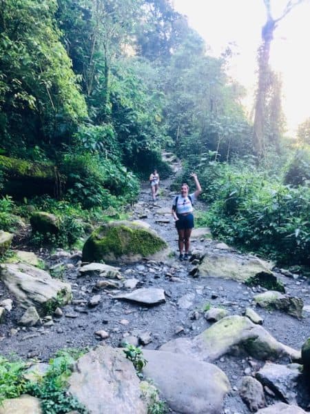 things to do in salento, salento colombia, cocora valley, valle de cocora, woman waving from the middle of a shallow stream filled with boulders