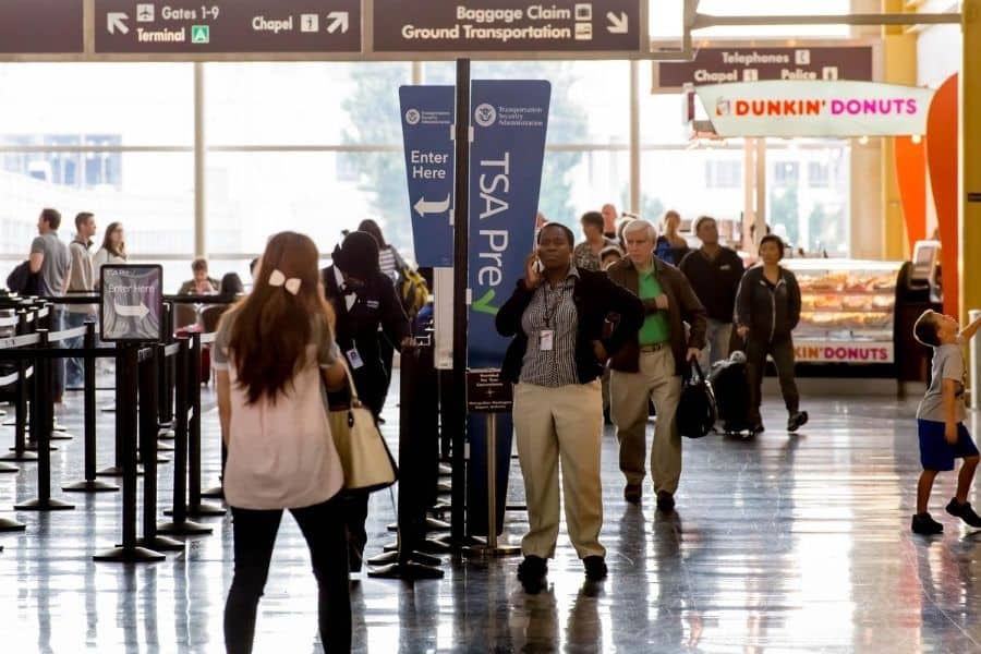 tsa precheck, trusted traveler programs, airport security, people standing in front of a tsa precheck sign and a dunkin donuts, easier travel, travel easier, travel hacks