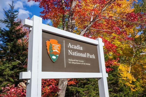 acadia national park entrance sign, fall trees in the background with yellow, red, and orange leaves, acadia hotels
