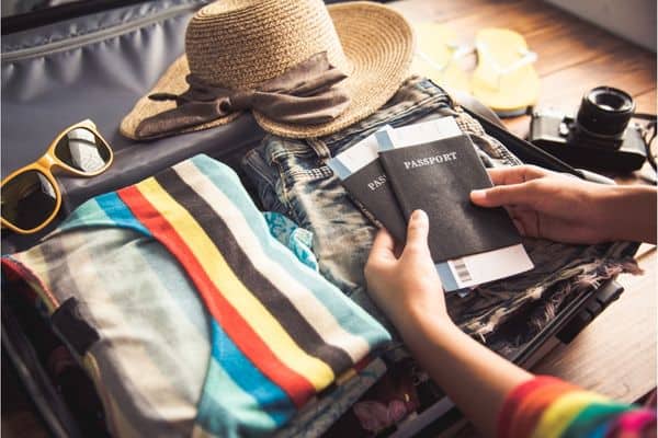 woman packing small bag, two passports, camera, sunglasses, clothes, hat, personal item packing list 