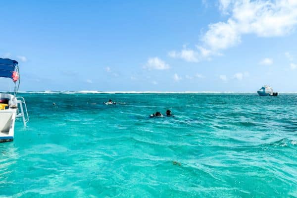 snorkelers in the water, bright blue water, boat in the distance, snorkeling ambergris caye, belize barrier reef, snorkeling belize barrier reef