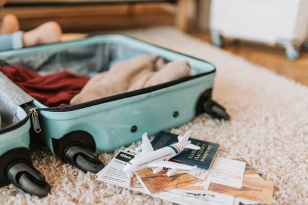Open suitcase with clothes in it, passport and tickets laying on floor, personal item packing list 