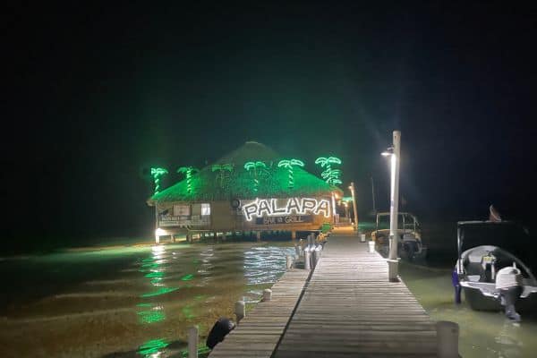 palapa bar at the end of the dock, bar lit up with green lights and green palm trees