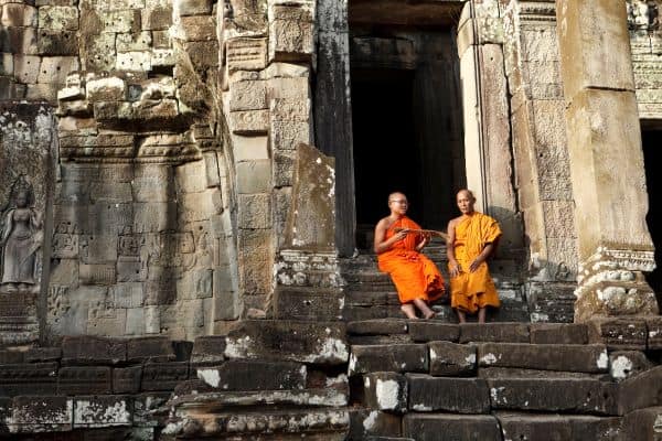 two monks wearing orange sitting on the steps of a temple in siem reap