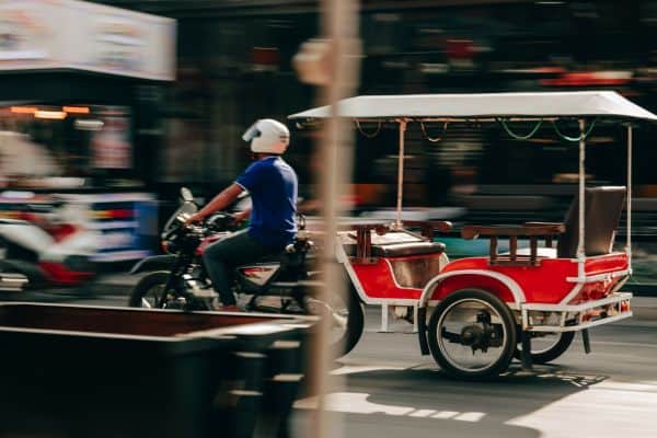 blurred picture of man driving tuk tuk through the street of siem reap, red tuk tuk, man on motorbike driving tuk tuk 