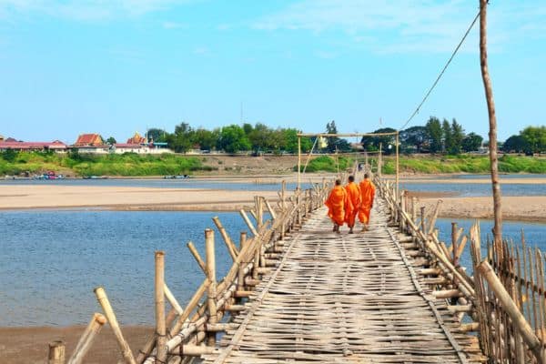 three buddhist monks dressed in orange crossing the bamboo bridge, kampong cham