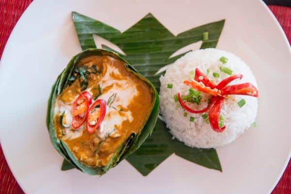 traditional khmer food in an upscale setting, ball of white rice with vegetables on top, curry wrapped in banana leaves with red peppers on top