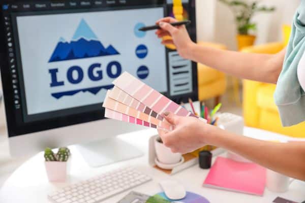 woman designing a graphic design logo on the computer, woman holding paint tablets, work from home side hustles, best passive income side hustles, start a side hustle