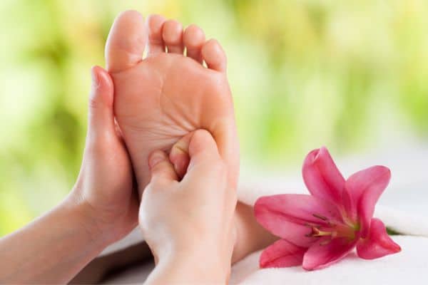 upclose photo of hands massaging a foot with a pink flower next to the foot, spa treatments dublin, refloxology massage