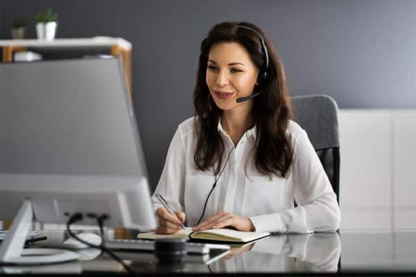 woman working as virtual assistant, woman sitting at desk talking on a headset and looking at a computer