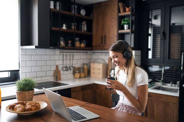 woman sitting at kitchen counter with headphones and drinking a cup of coffee, computer on the counter, side hustles, best passive income side hustles, side jobs from home