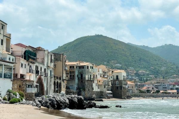 view of the oceans and mountains in cefalu, homes and buildings right by the ocean, pier in the distance