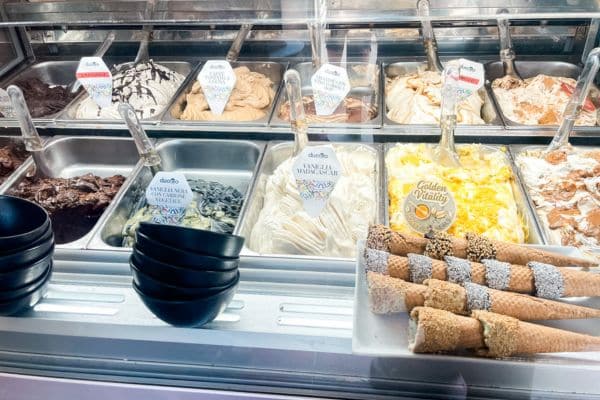 glass case showing all the different flavors of gelato, cones with toppings on them on the right side, black bowls on the left side 