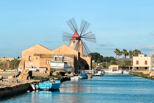 view from the boat coming into the marsala salt flats, boat docked along the pier, large windmill standing out, saline di marsala, marsala salt flats 