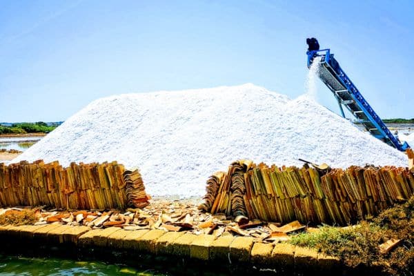 large pile of salt, man on top of device that is dumping more salt onto the pile, marsala salt pans 