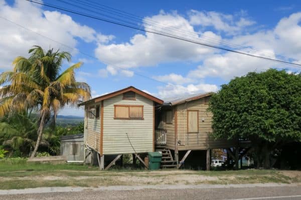 two belizian houses with palm trees, blue sky with clouds, mountains and fields in the distance, best places to stay in san ignacio belize, where to stay in san ignacio