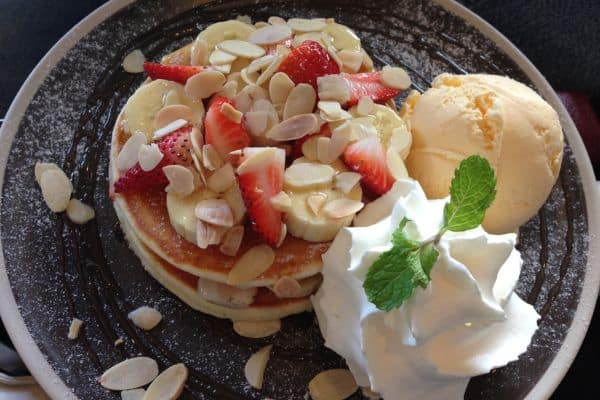 american pancakes topped with bananas, strawberries, and shaved nuts, whipped cream and ice cream on the side