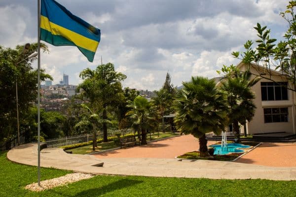 genocide memorial kigali, rwanda flag blowing in the breeze, memorial building surrounded by trees, buildings and hills in the distance