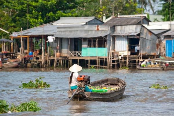 woman sitting on boat with small motor sailing towards houses on stilts in the mekong delta