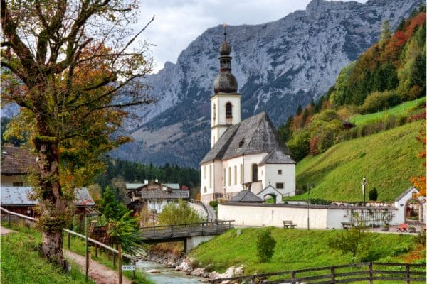 old church in berchtesgaden, green hills with trees with leaves changing colors, snow covered mountains in the background, weekend trips from munich
