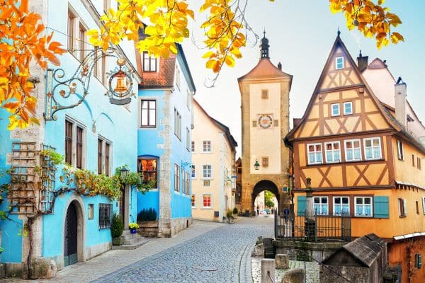 orange and yellow leaves in front of the camera, blue and orange buildings, town square of old german town