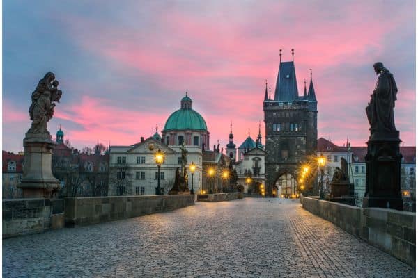 purple and pink sunset over the streets of prague, statues on either side of the street, street lamps glowing, day trips from berlin, weekend trips from berlin