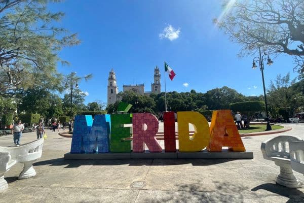 colorful merida sign with mexico flag flying in the background, small town square, things to do in merida yucatan, places to see in merida