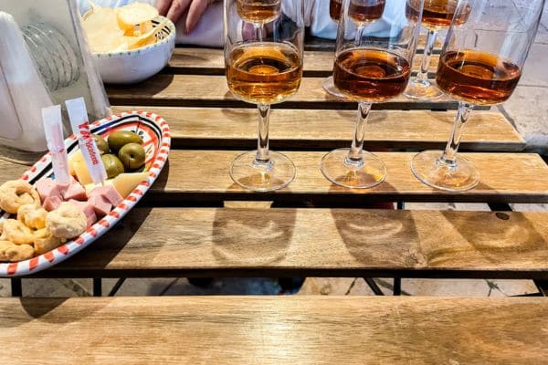 wine tasting, three glasses filled with wine next to a small plate of olives and cheese, marsala wine sicily, marsala italy 