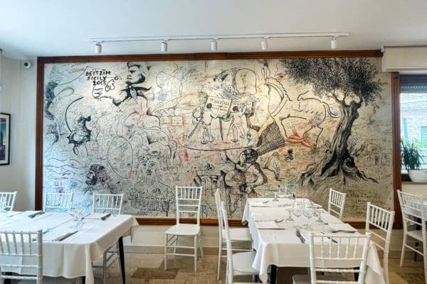 inside one of the restaurants in marsala, big mural painting on the back wall, white chairs and tables covered with white tablecloths 