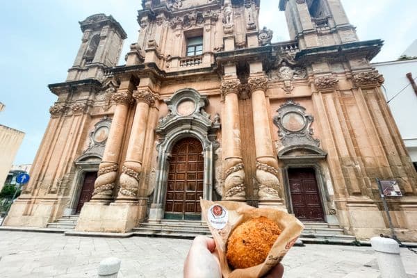 me holding an arancina in front of one of the old buildings in the historic part of the city