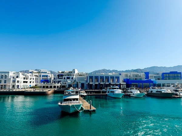 stunning blue water of the red sea with mountains and buildings in the background, boats floating in the water